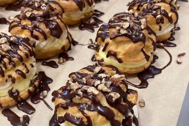 Chocolate-drizzled cream puffs topped with nuts on a baking sheet from Sierra Bakehouse